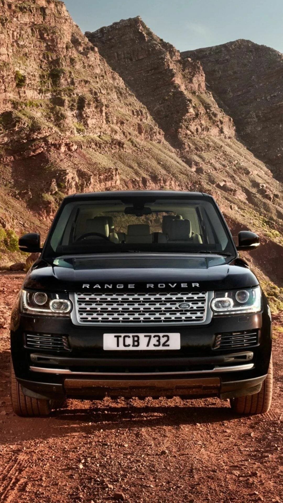 Front view of a black Range Rover SUV on a dirt road with massive rocky cliffs in the background.
