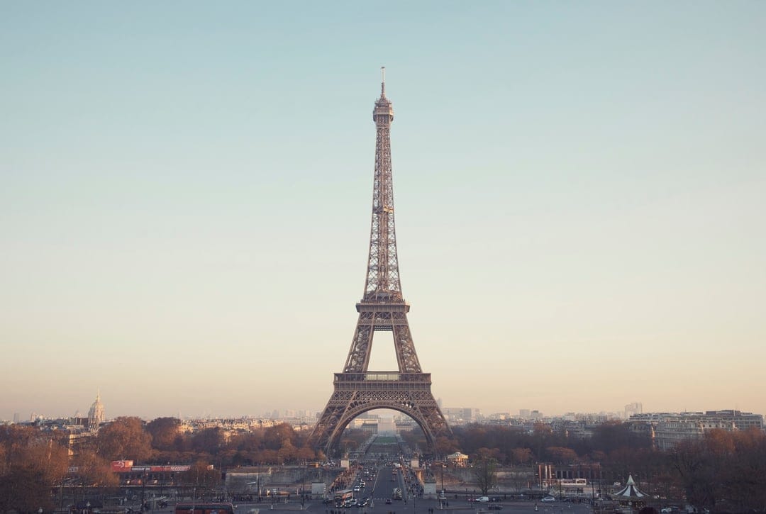 Eiffel Tower stands amidst a golden sunset glow over the Paris cityscape with a soft hazy sky background.