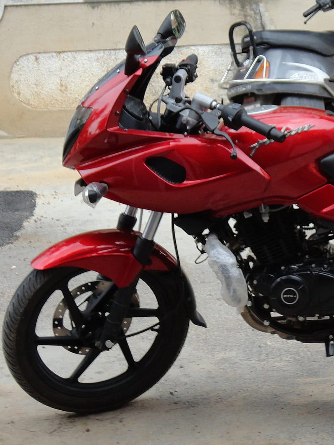 Red motorcycle fairing with dual headlights above a black alloy wheel and disc brake on a sportbike.