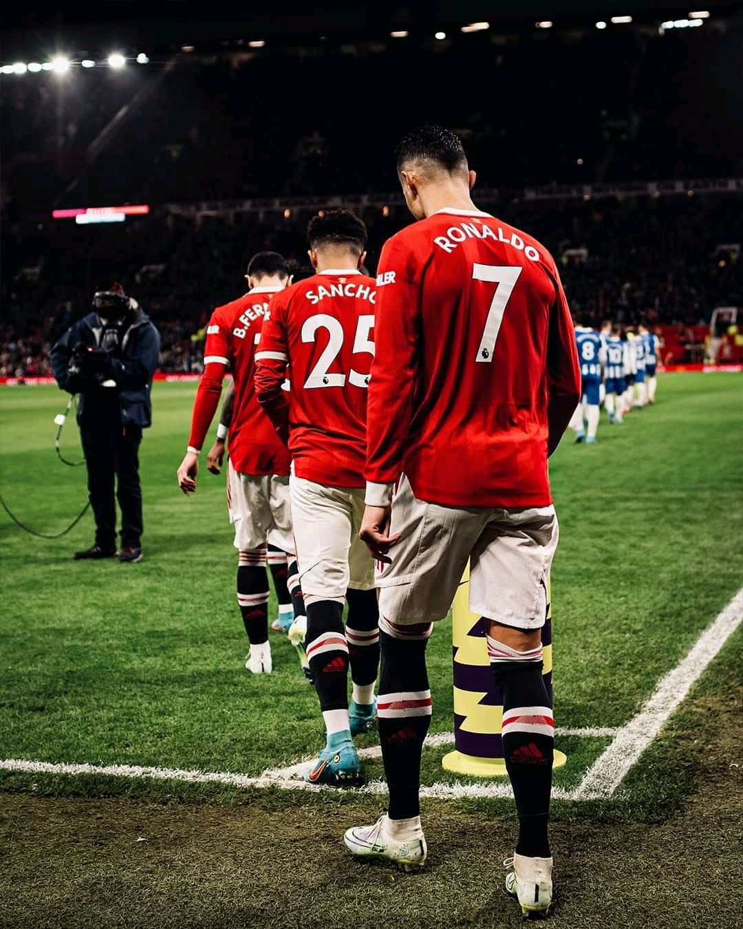 Cristiano Ronaldo and teammates in red jerseys walk off a lit football pitch toward a cameraman in the distance.