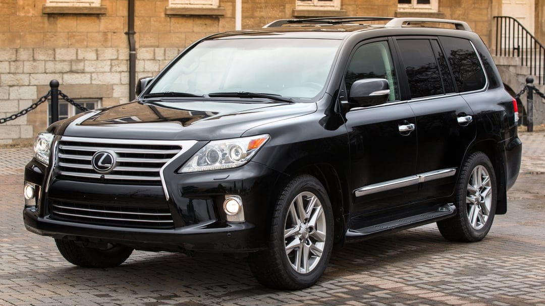 Black Lexus LX 570 SUV parked on a cobblestone path in front of a tan stone building in daylight.