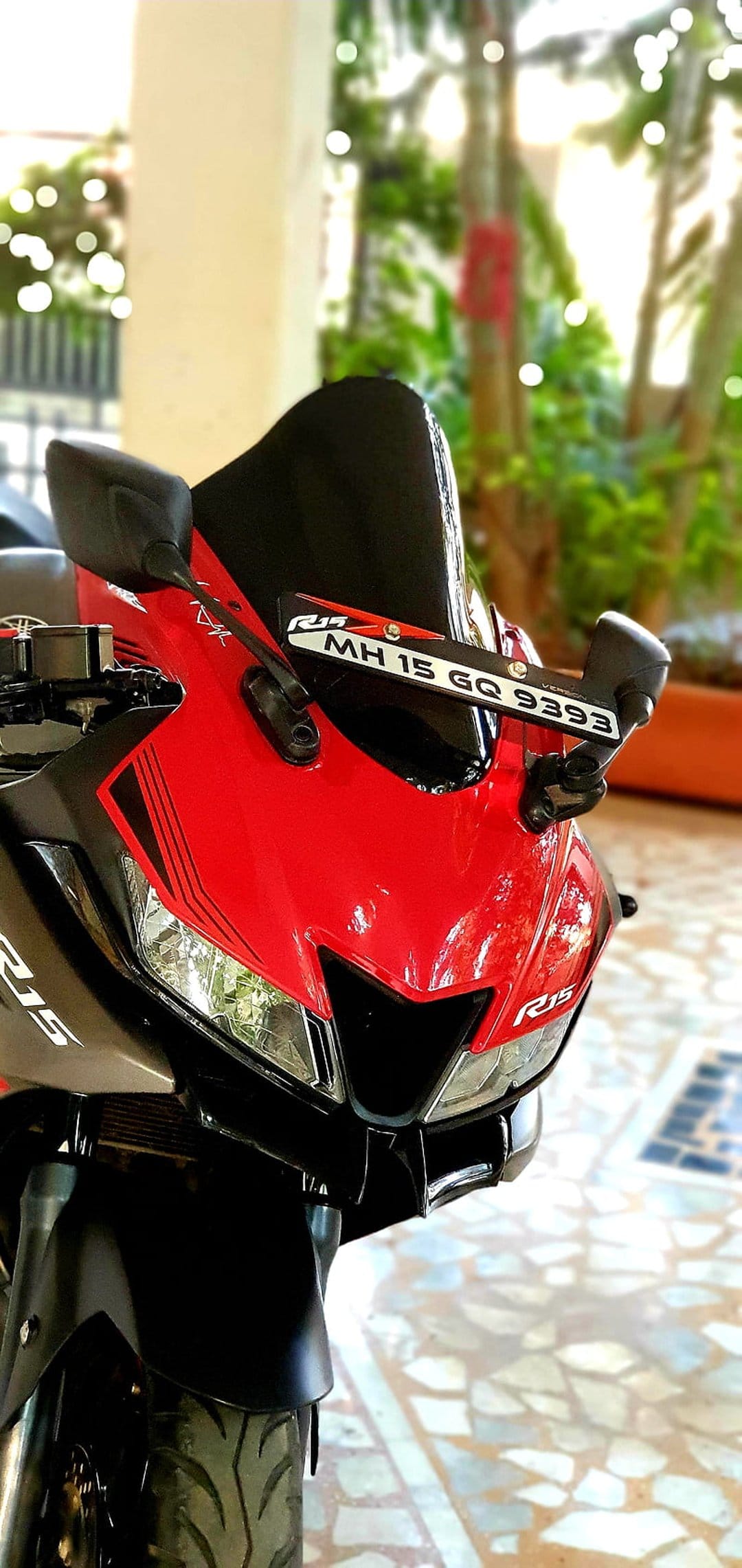 Red Yamaha R15 motorcycle front fairing with sharp headlights and black windscreen against blurred green trees.