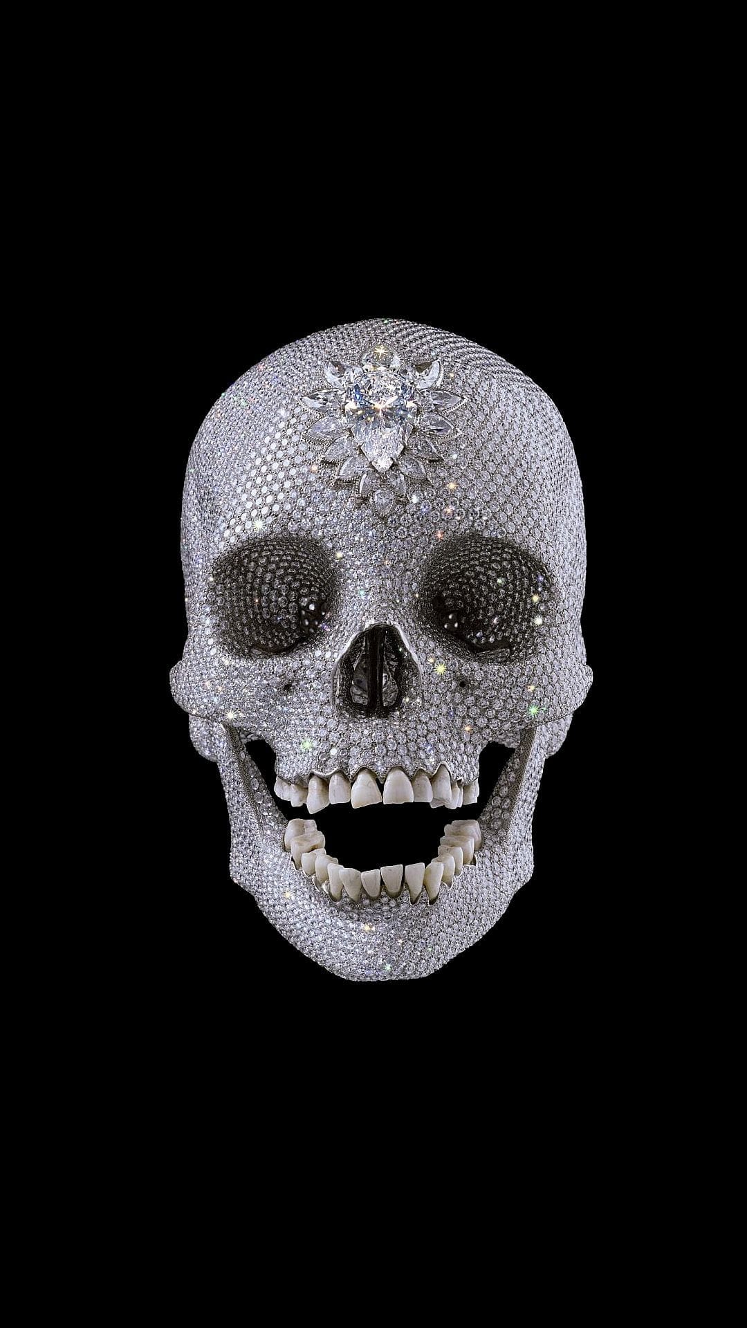 Human skull encrusted with shimmering diamonds featuring a floral gemstone star emblem against a dark background.