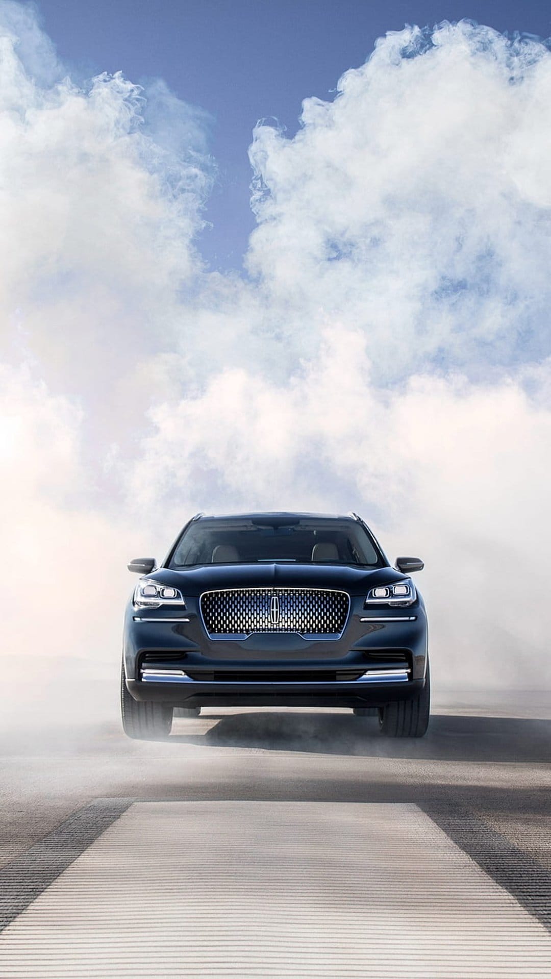 Black Lincoln Aviator SUV driving through a thick dust cloud with its headlights glowing against a hazy sky.