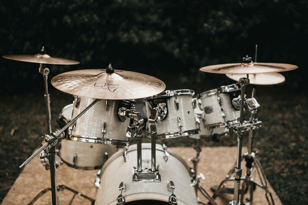 White drum kit with polished brass cymbals stands in soft outdoor light, showing detailed metallic hardware textures.