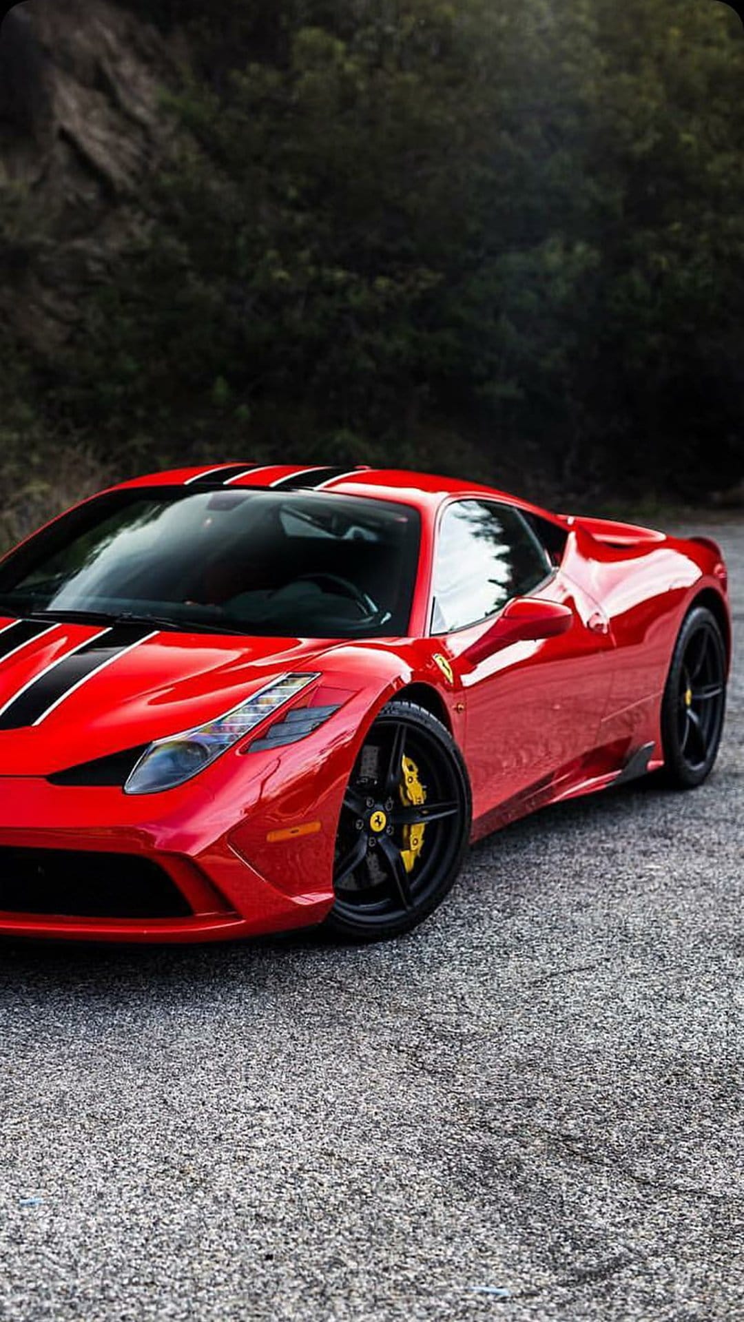 Red Ferrari 458 Italia with black stripes and yellow calipers parked on asphalt with a blurred tree background.