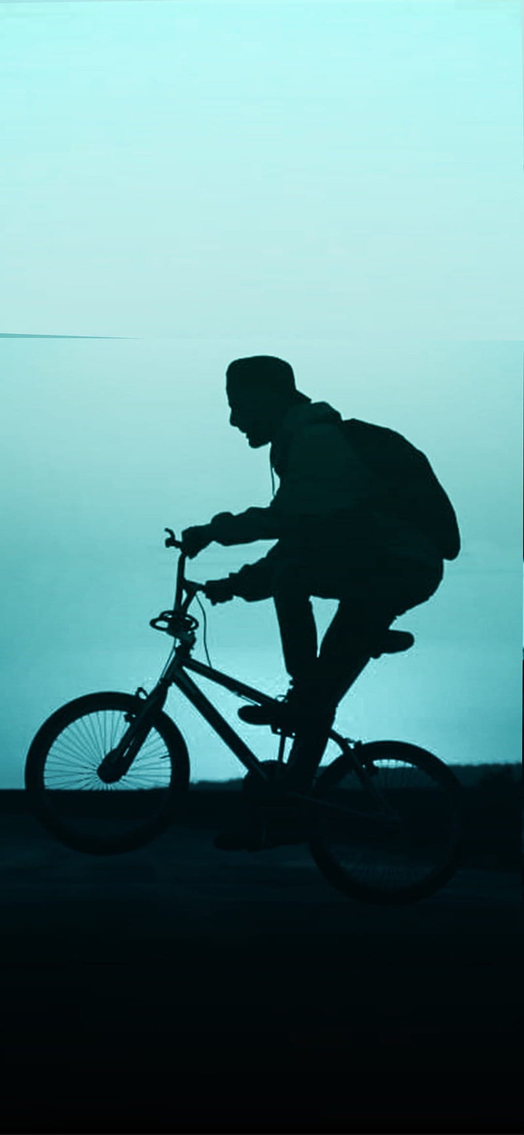 BMX cyclist in silhouette performs an aerial trick against a vast, bright cyan sky with a soft color gradient.
