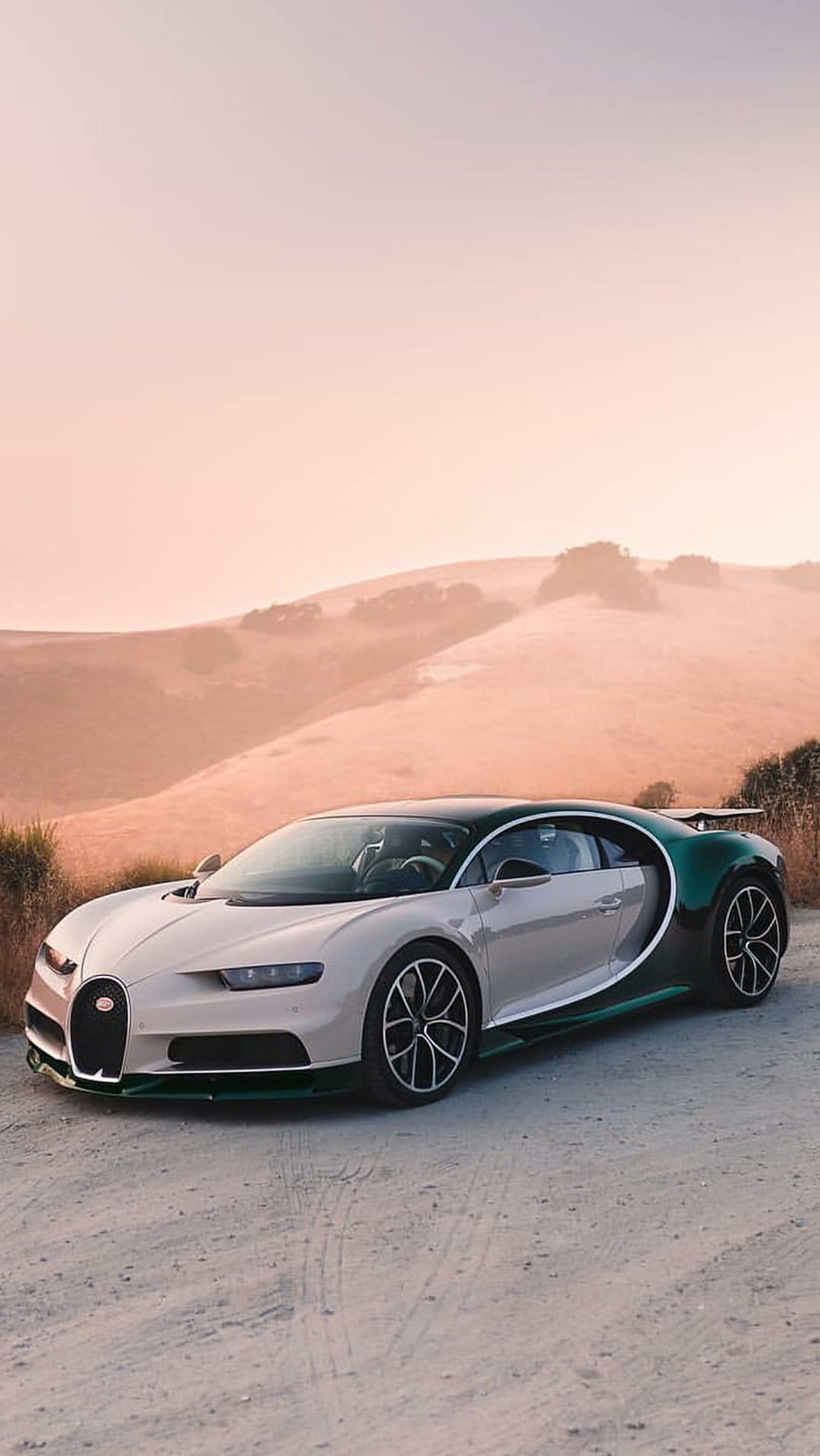 Bugatti Chiron in emerald and beige parked on a dirt road against rolling hills under a purple sunset sky.