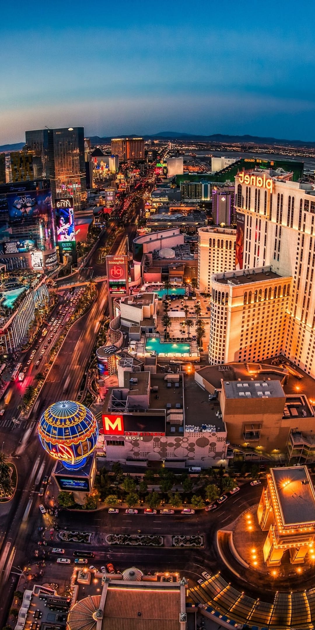 Las Vegas Strip hotels and the High Roller wheel glow with neon lights under a twilight sky at dusk.