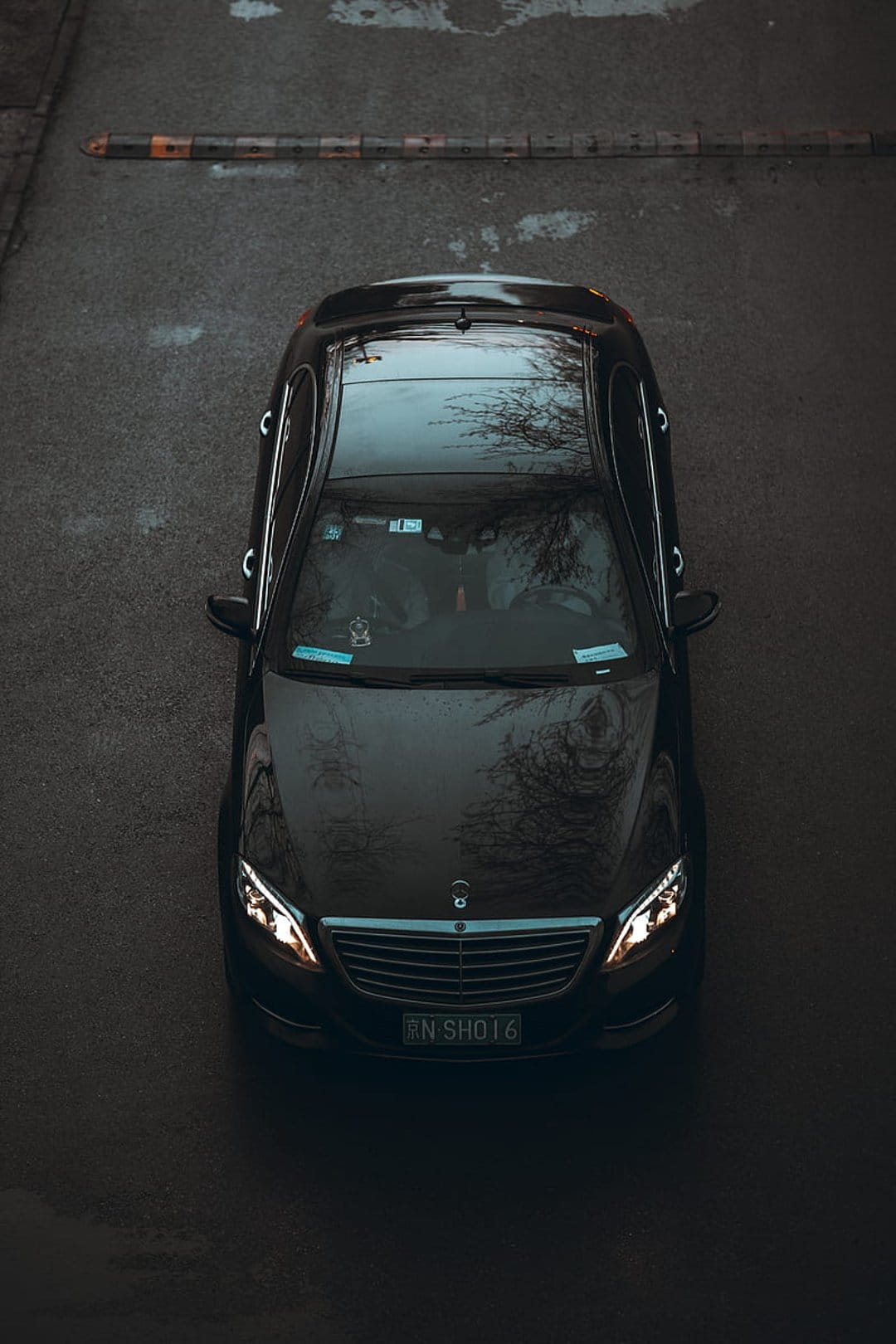 Black Mercedes S-Class luxury sedan parked on wet asphalt seen from a high overhead bird's-eye perspective.