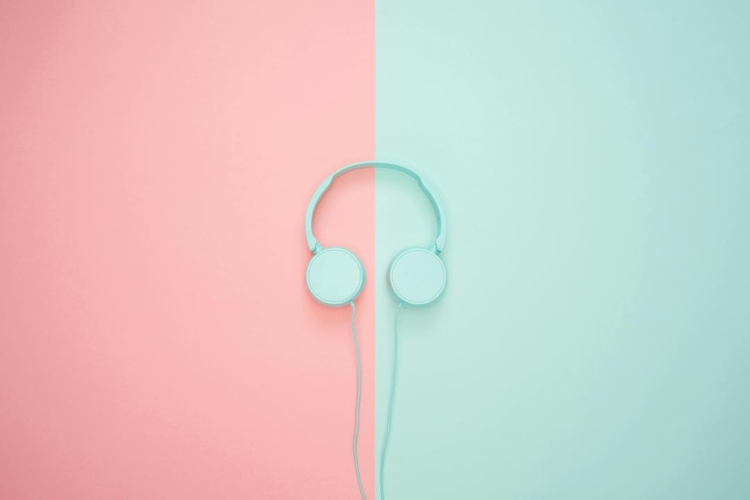 Blue minimalist headphones centered on a vertical split background of pastel pink and soft teal surfaces.