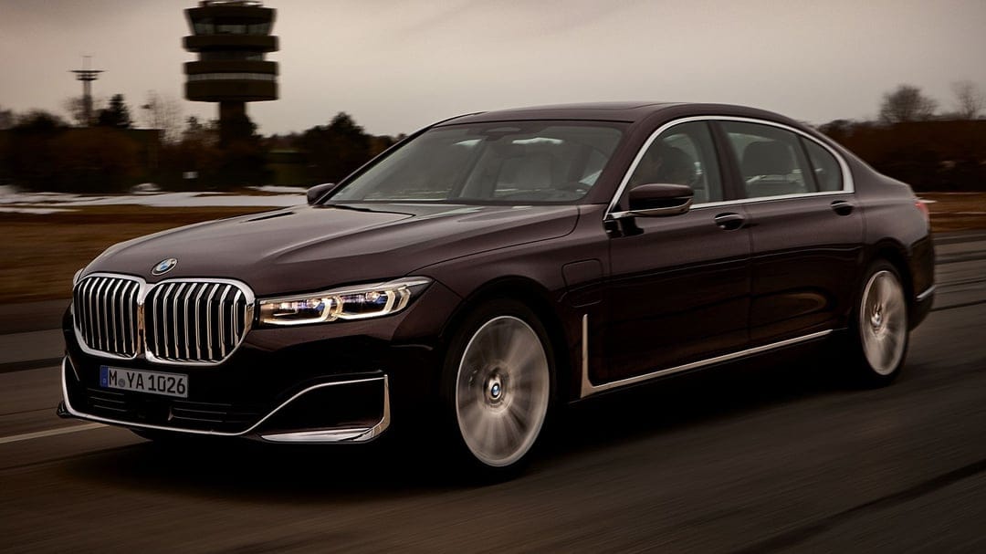 Dark purple BMW 7 Series sedan driving past a tall control tower under a moody evening sky with motion blur.