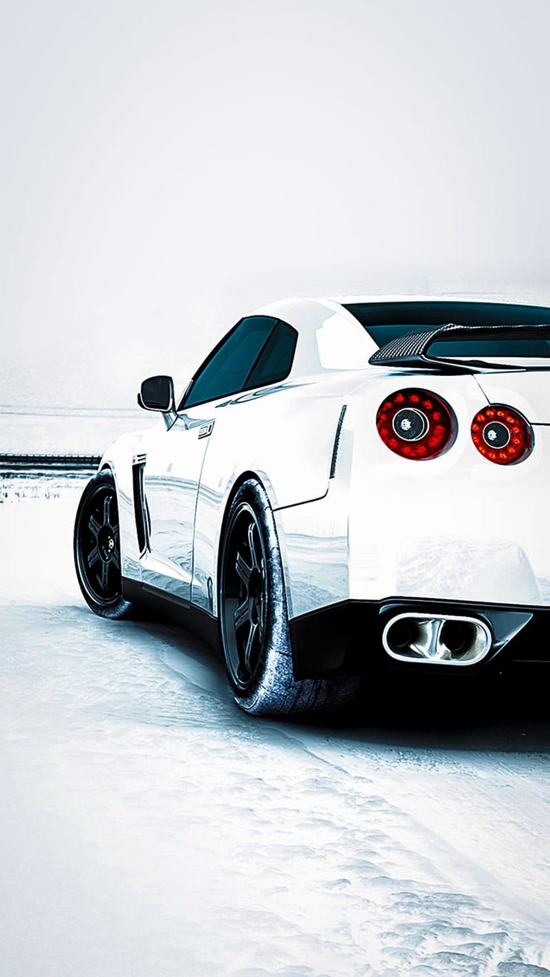 Nissan GT-R rear view with round red taillights and dual exhausts parked on a pristine white snow field.