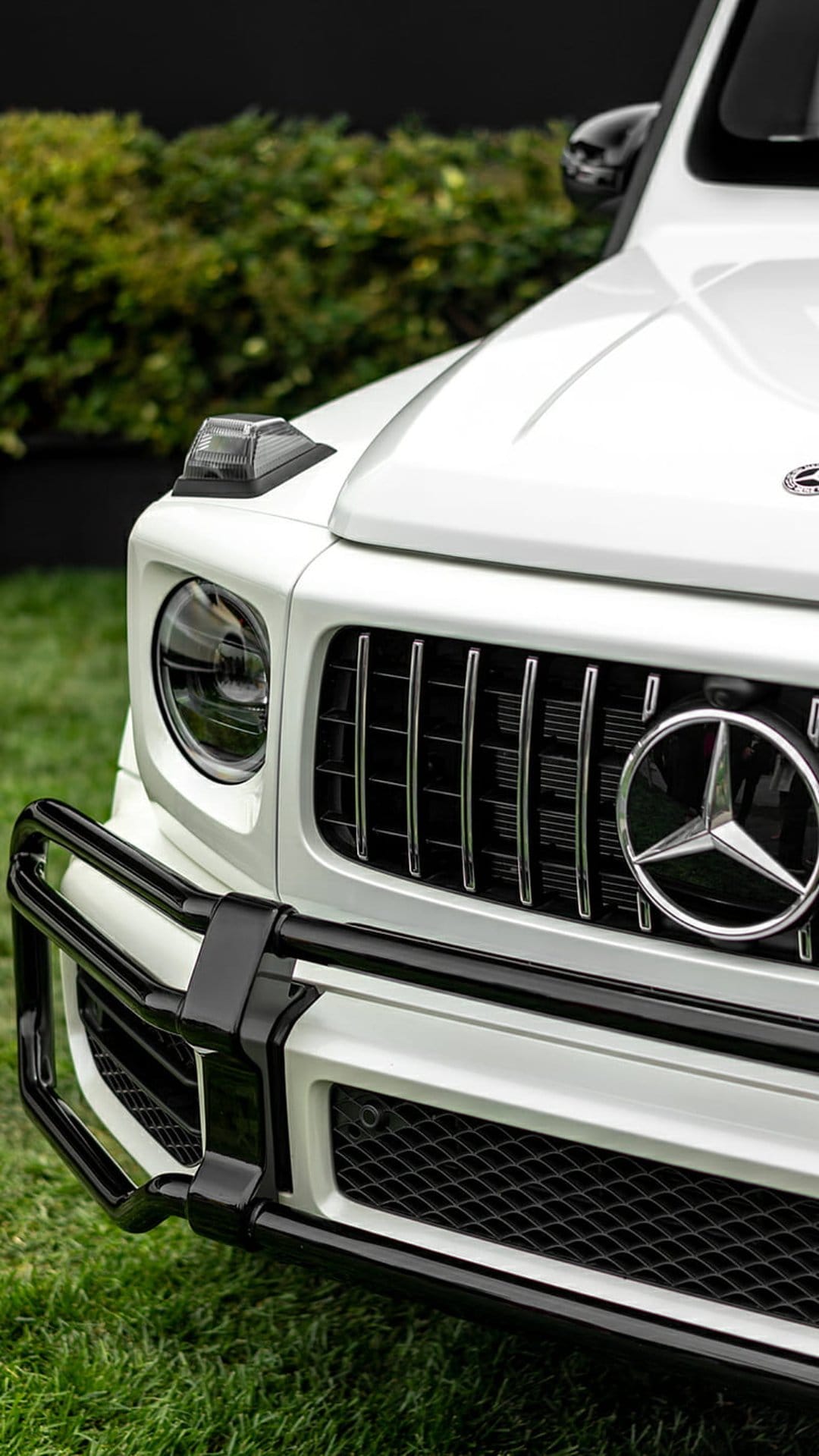 Mercedes-Benz G-Class grille with chrome star emblem, round headlight, and black bumper over green grass.