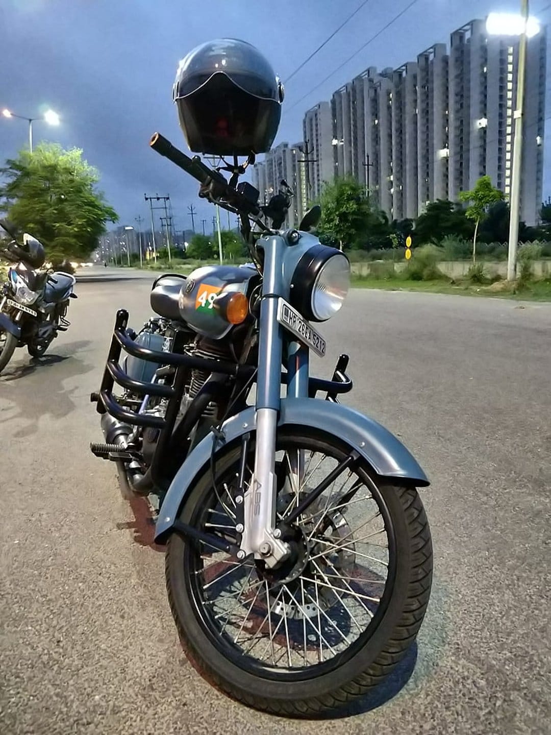 Royal Enfield motorcycle with a black helmet on the handlebars parked on a city road against twilight buildings.