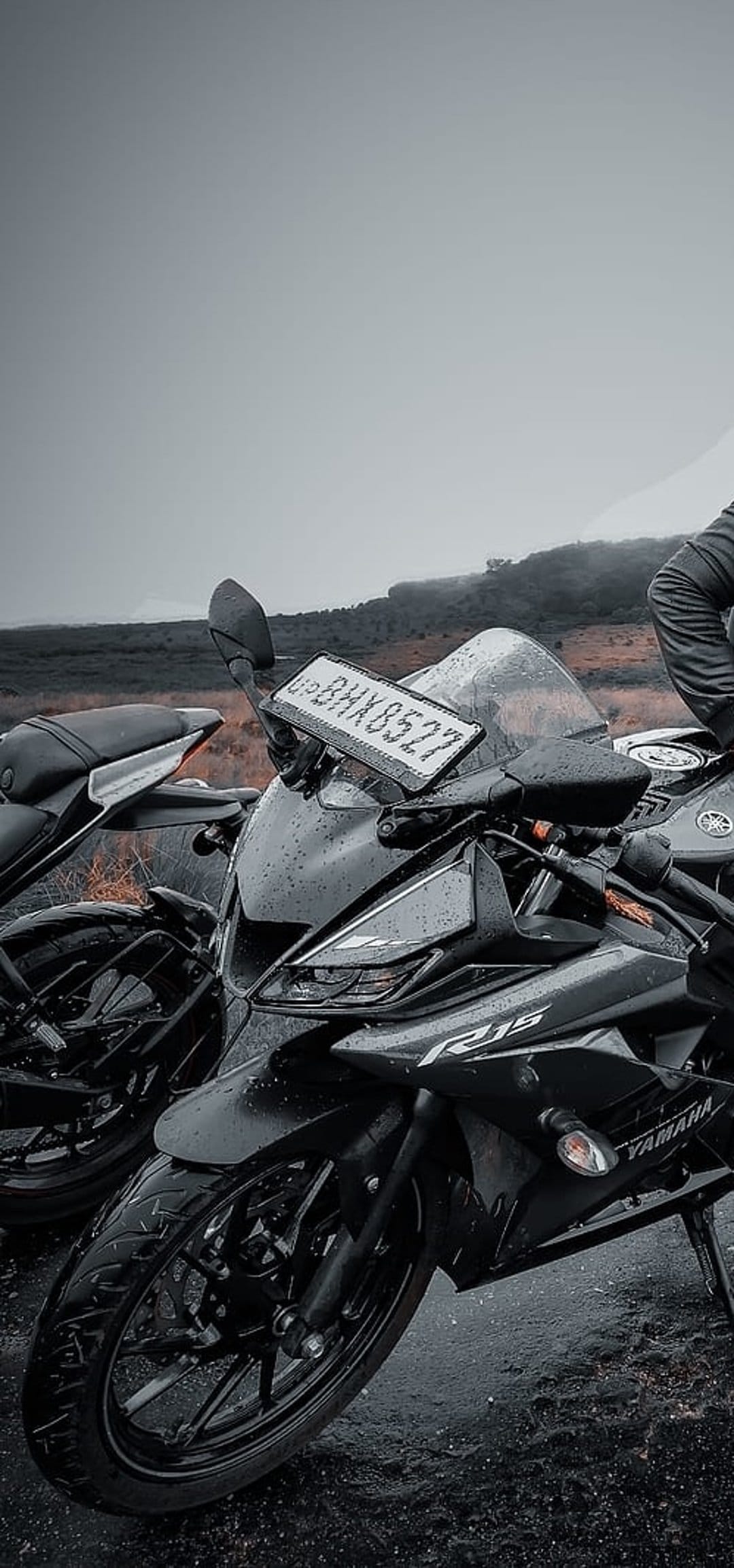 Black Yamaha R15 V3 motorcycle on wet asphalt under a misty sky, showcasing sleek fairings and rainy reflections.