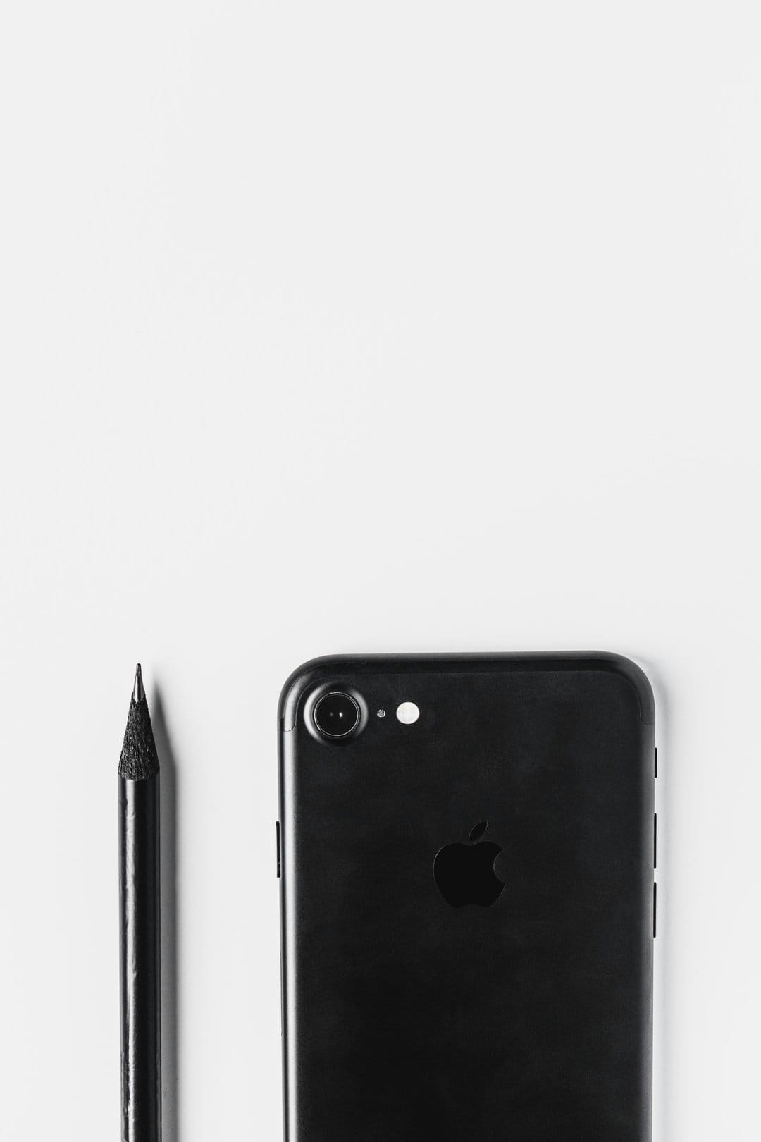 Black smartphone and graphite pencil lie on a white background in a minimalist overhead flat lay composition.
