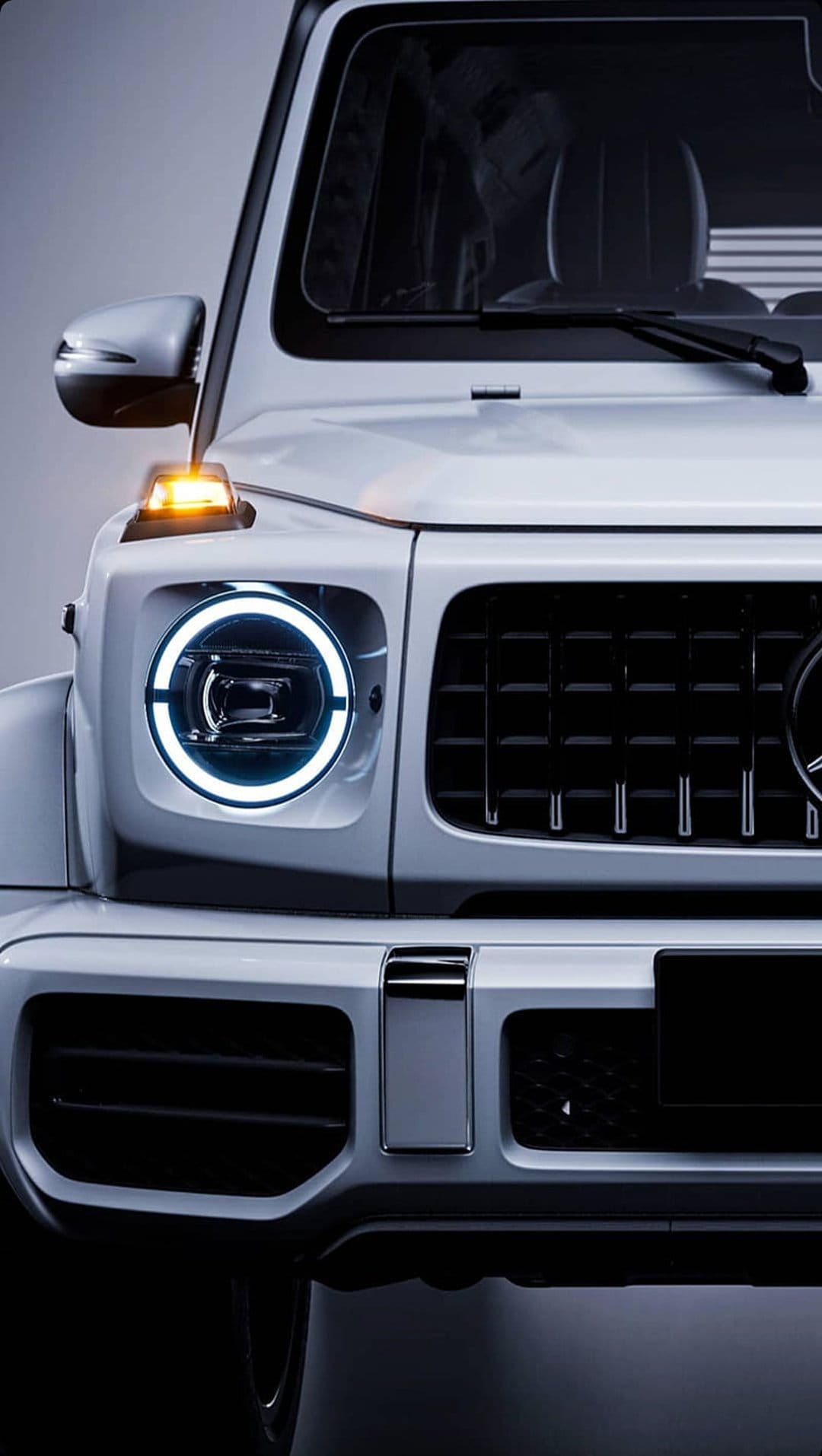 White Mercedes G-Class SUV highlights circular LED headlights and a black grille in a vertical close-up shot.