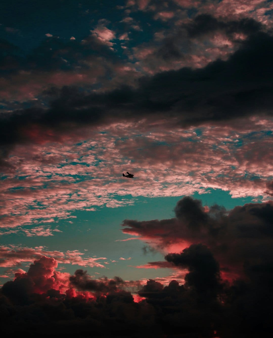 Helicopter silhouette flying through vibrant orange and pink clouds during a dramatic teal twilight sunset.