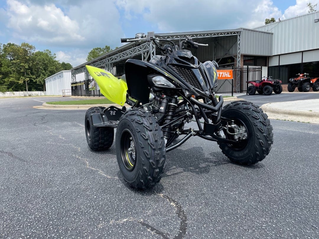 Black and lime green Yamaha Raptor sport ATV parked on an asphalt lot under a bright cloudy sky.