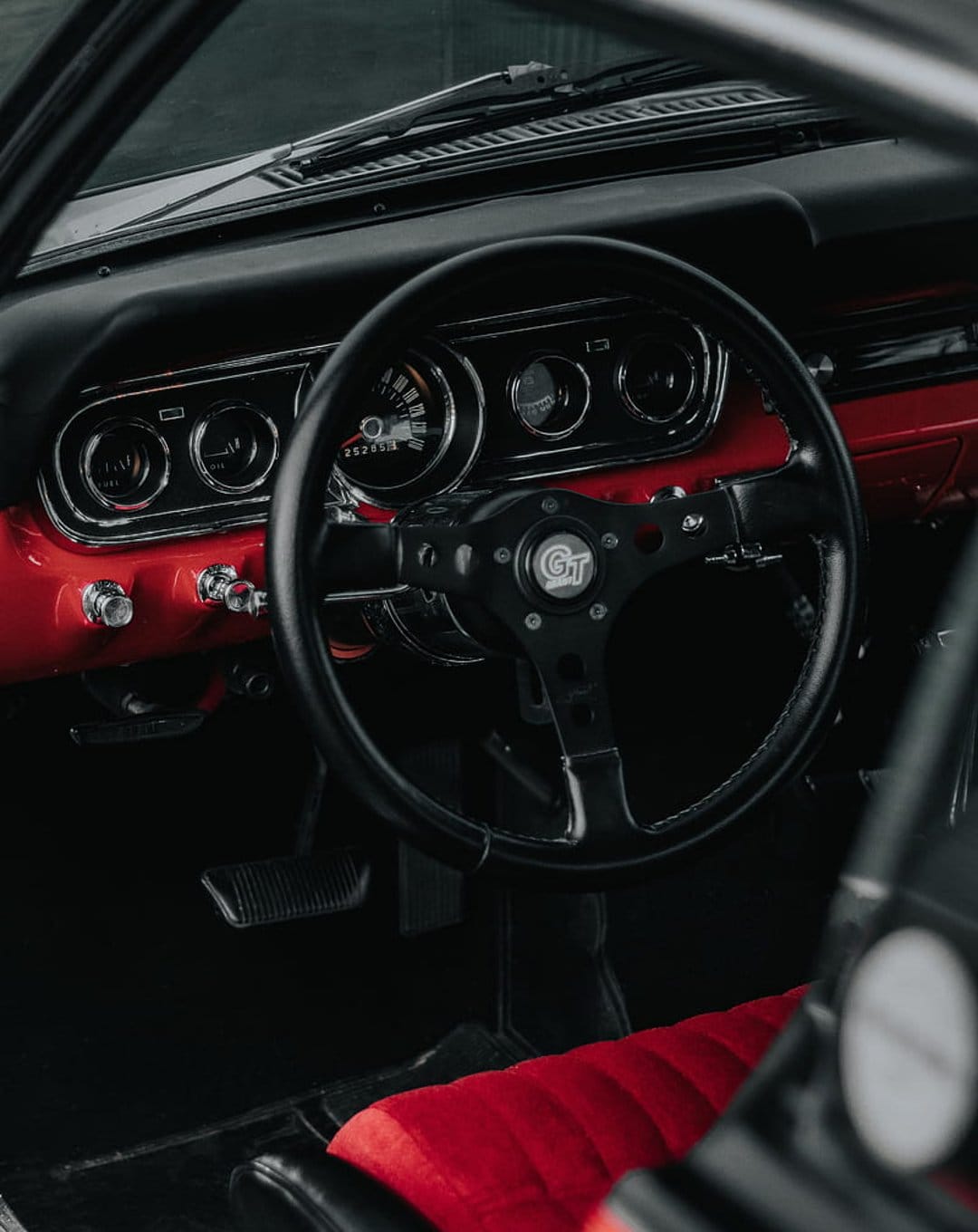 Black GT steering wheel and red dashboard with chrome analog gauges and matching leather car seat upholstery.