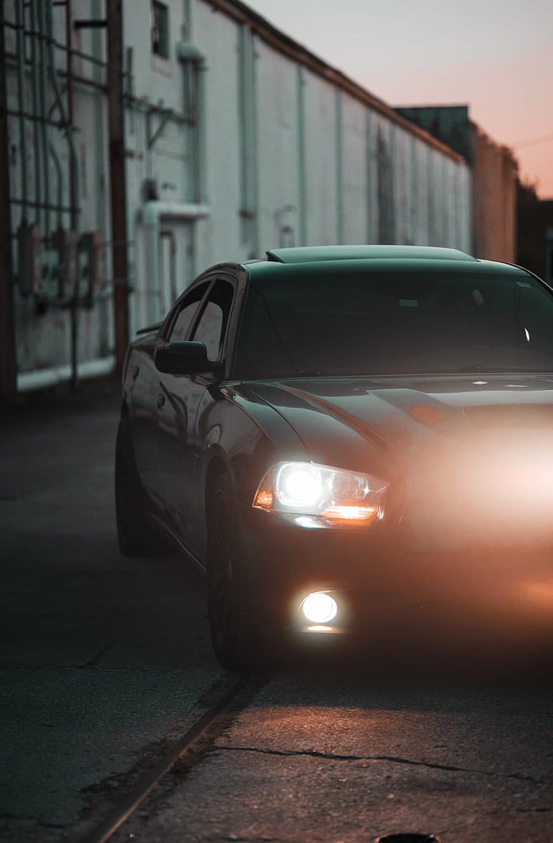 Dodge Charger with glowing LED headlights parked in a dark, foggy urban alleyway at night between brick walls.
