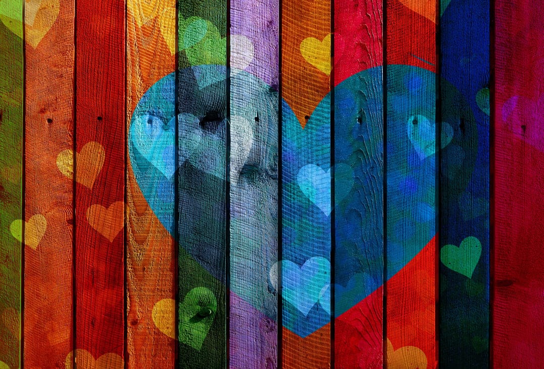 Large blue heart sits atop colorful vertical wooden planks with small floating hearts and visible wood grain.