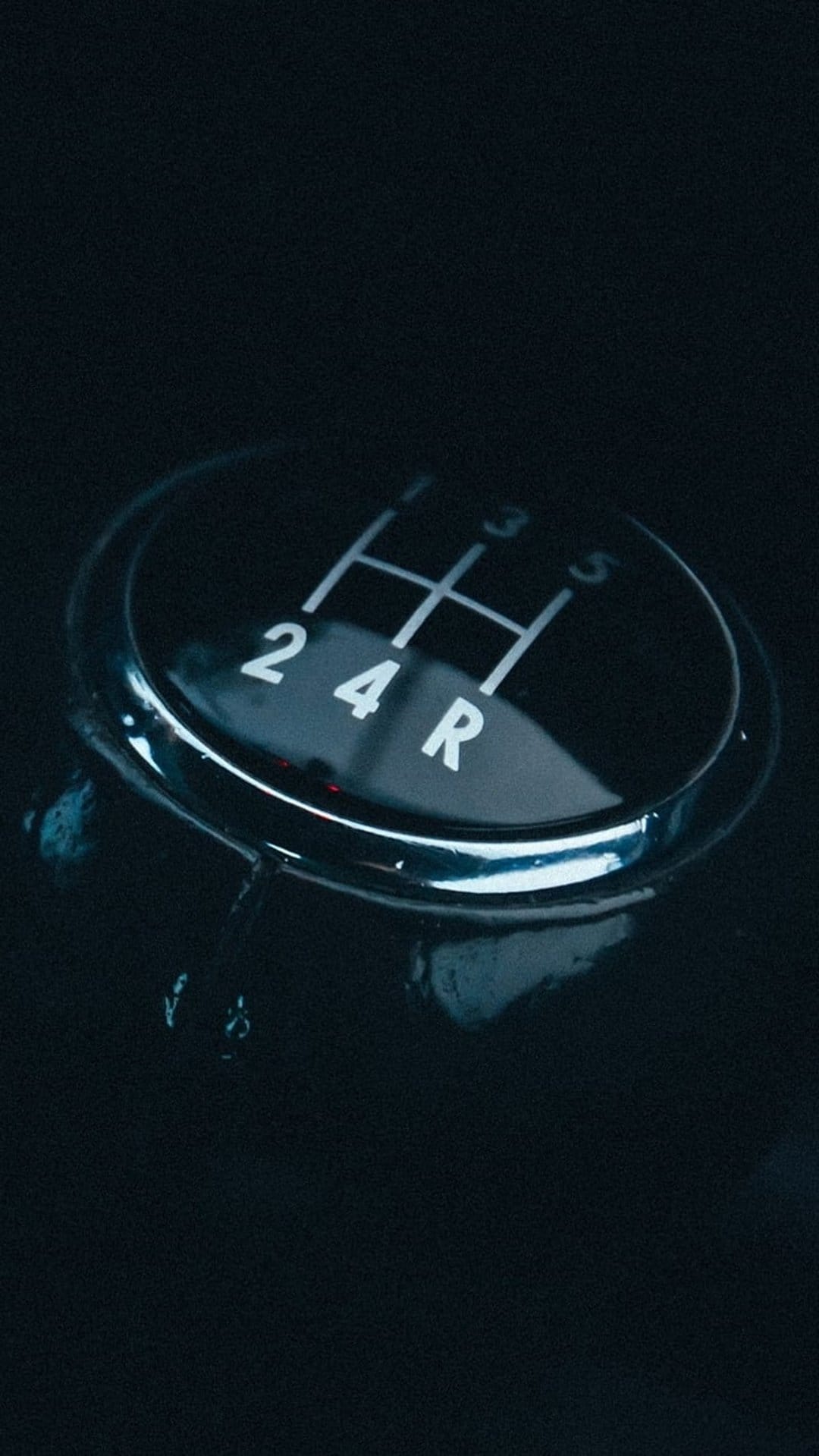 Manual five-speed gear shift knob with white illuminated numbers and a polished chrome trim in a dark car interior.