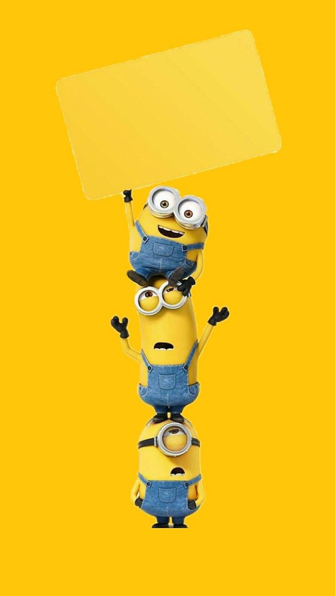 Three Minions in denim overalls stacked vertically against a yellow wall with the top one holding an empty sign.