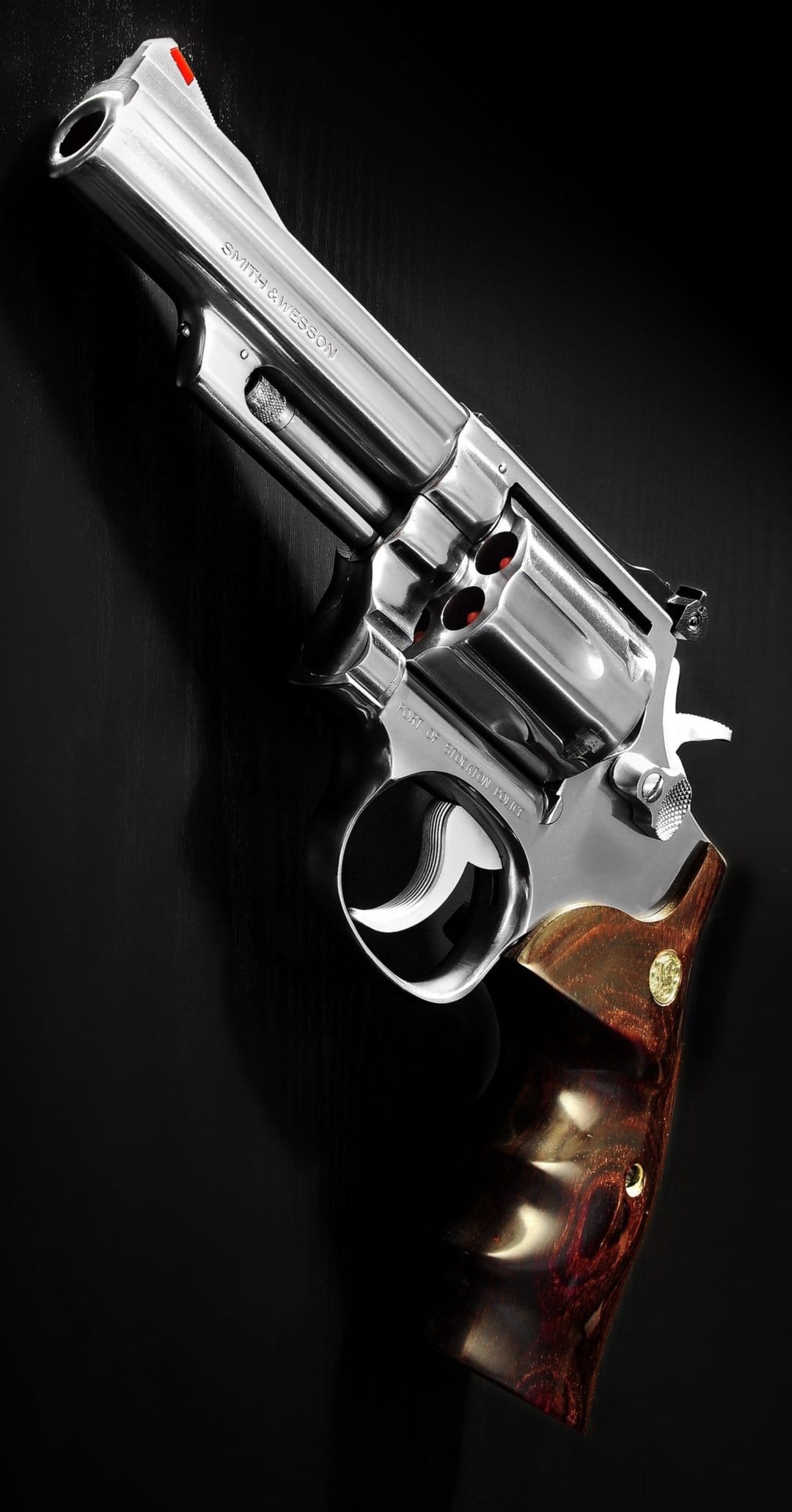 Silver revolver with a brown wooden handle and red-tipped cartridges laying on a reflective black surface.