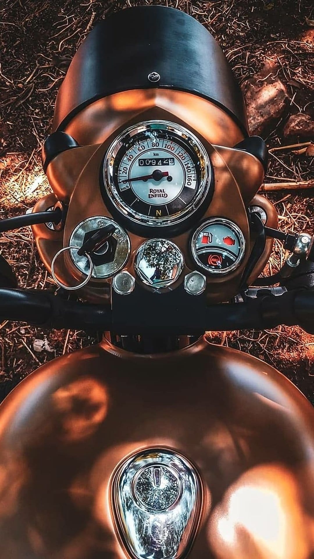 Classic motorcycle speedometer and odometer set against a polished copper fuel tank in a dark environment.