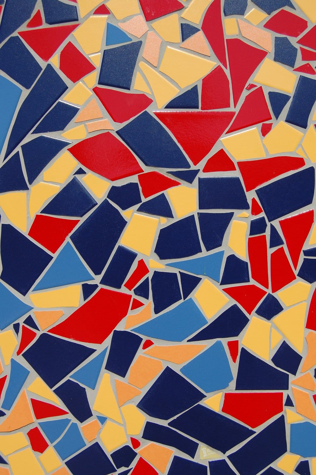 Fragmented ceramic tiles in blue, red, and yellow form a textured mosaic pattern with gray grout lines.