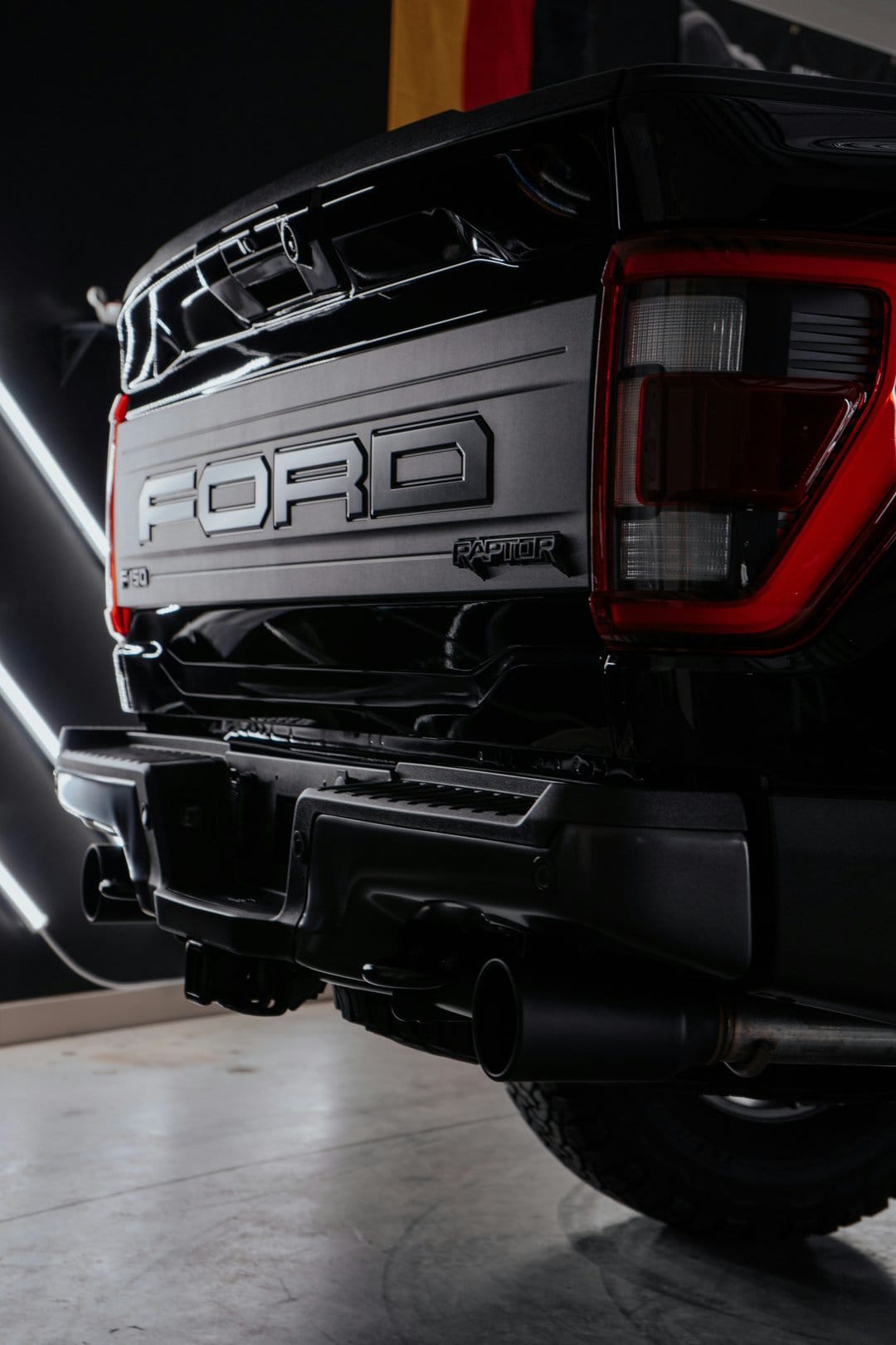 Black Ford F-150 Raptor tailgate with dual exhaust pipes and glowing red LED taillight accents in close-up.