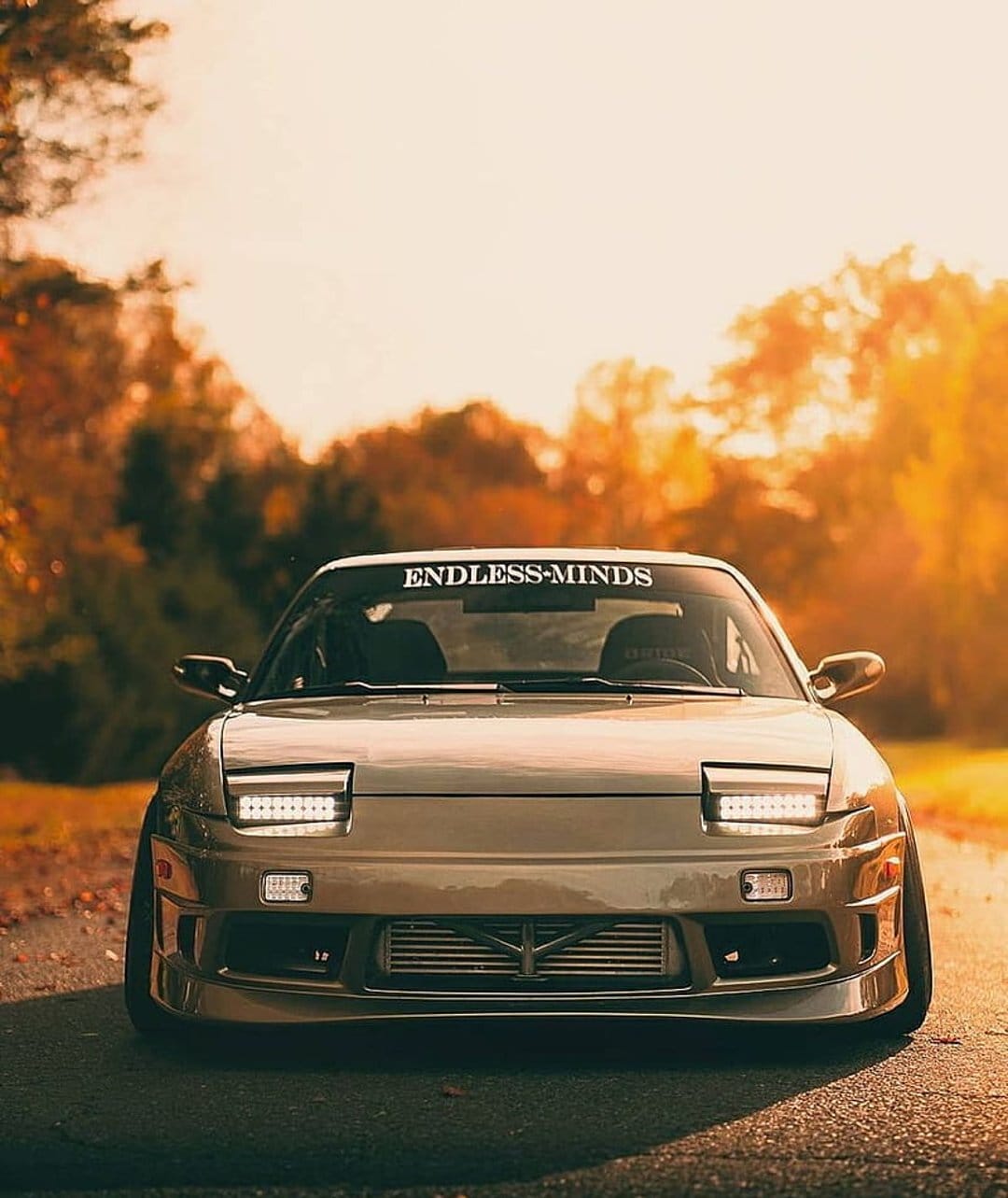 Nissan 240SX S13 Silvia with LED lights and exposed intercooler parked on a road during a golden autumn sunset.
