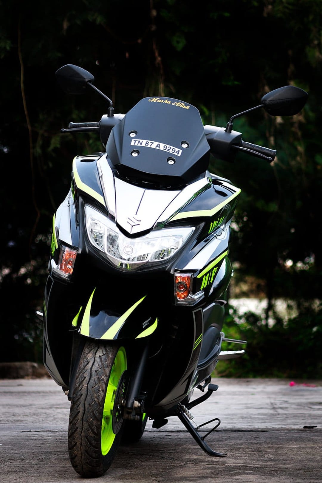 Suzuki Burgman scooter with neon green wheels and racing decals parked against a blurred forest background.