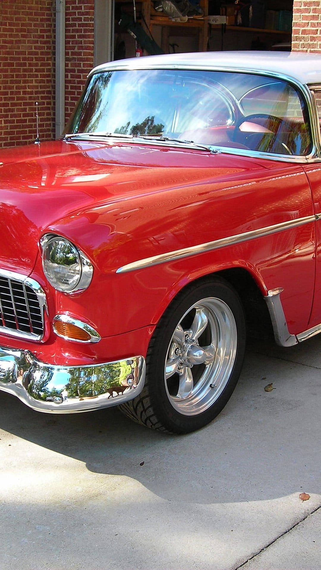 Red 1955 Chevrolet Bel Air front grille and chrome bumper with circular headlights and custom shiny wheels.