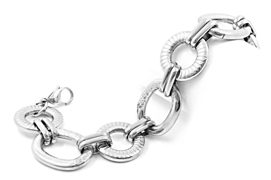 Silver chain bracelet featuring ribbed circular and smooth oval links displayed on a neutral surface.
