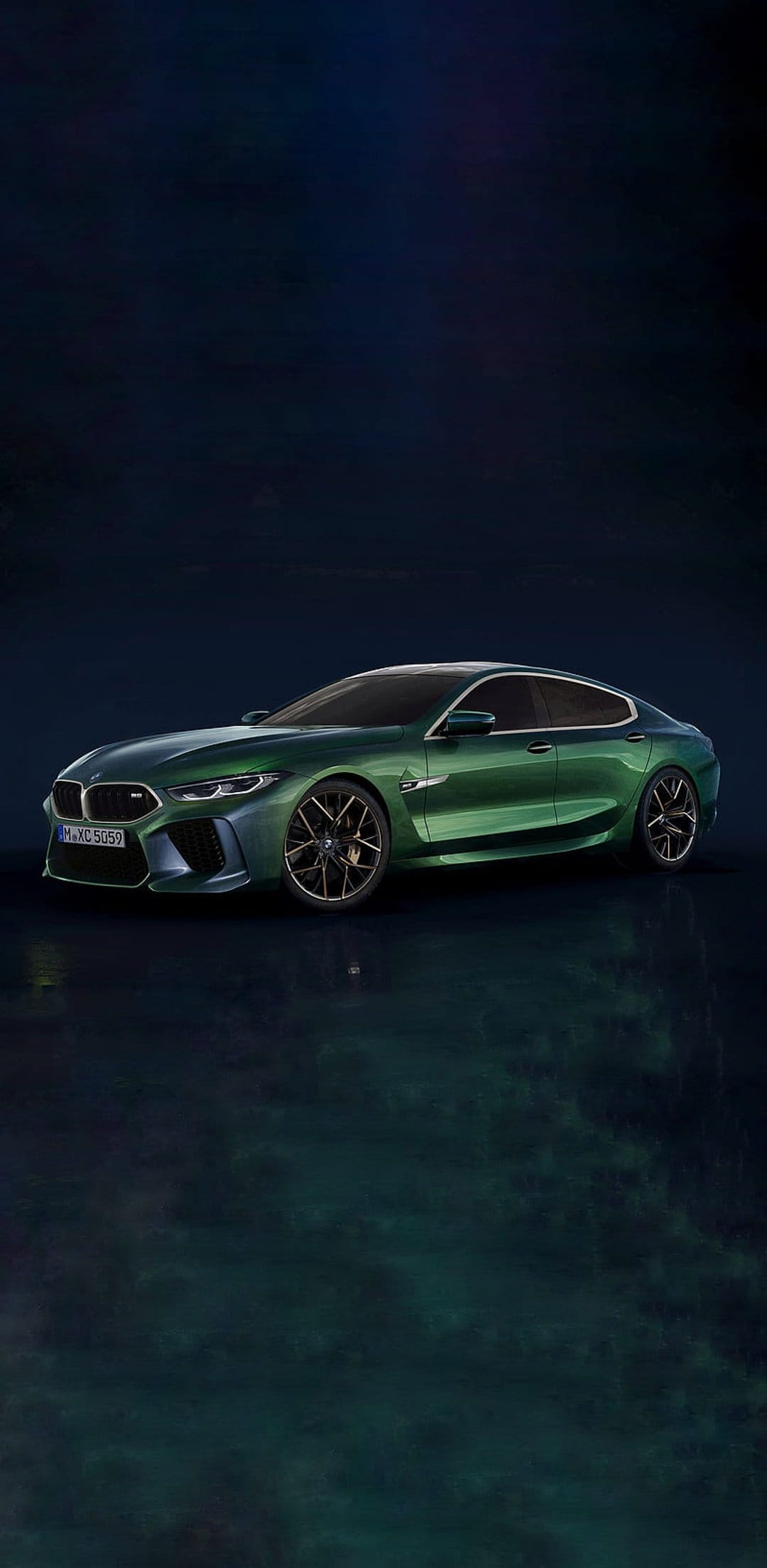 BMW M8 Gran Coupe in metallic green parked on a dark reflective floor with dramatic studio lighting and shadows.