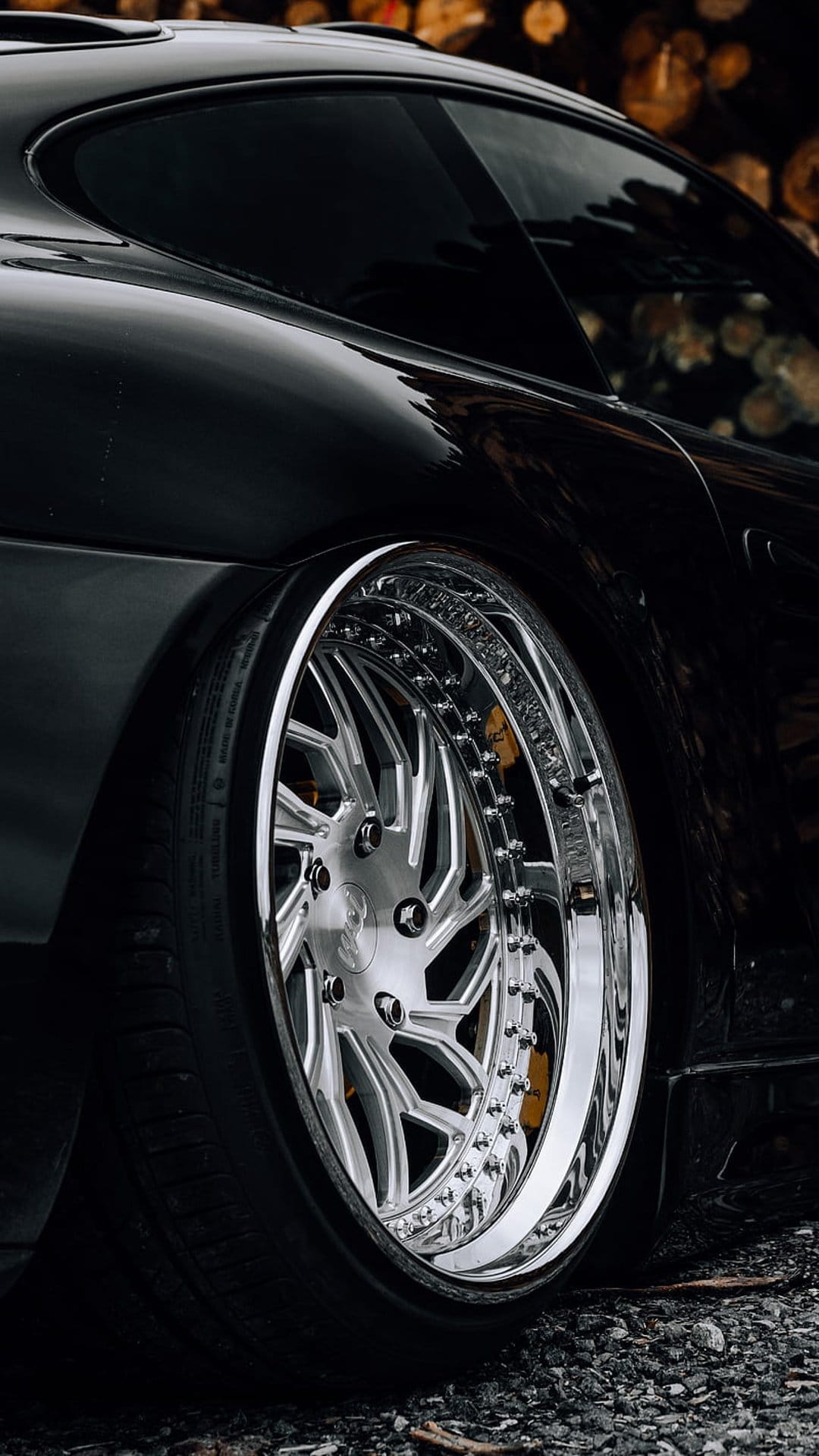 Polished chrome multi-spoke wheel with yellow brake calipers on a lowered black car with blurred bokeh lights.