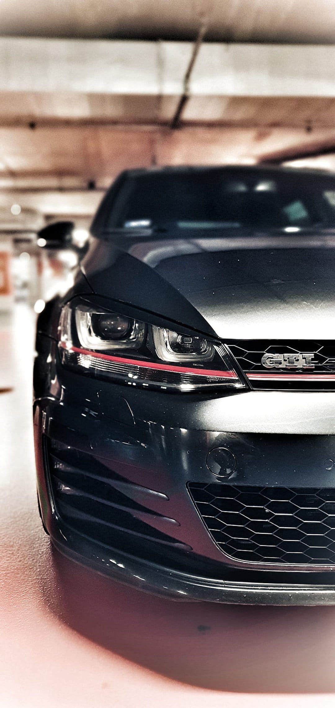 Dark grey Volkswagen Golf GTI front grille and headlights with red trim in a low-angle garage close-up.