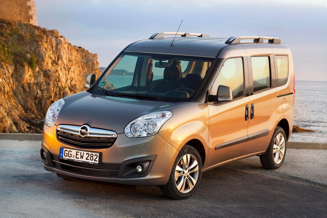 Bronze Opel Combo MPV parked on a coastal road at sunset with rocky cliffs and the sea in the background.
