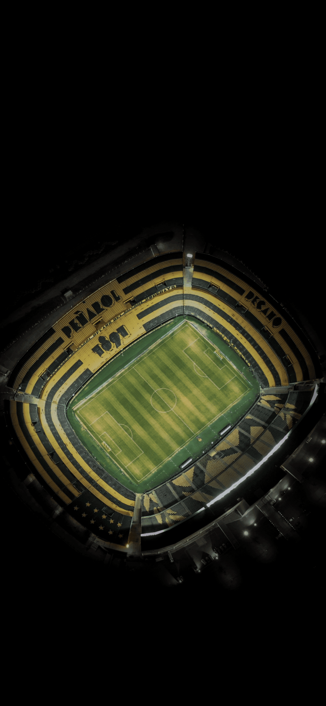 Football stadium at night with yellow and black seats, a green pitch, and Peñarol branding from an aerial view.
