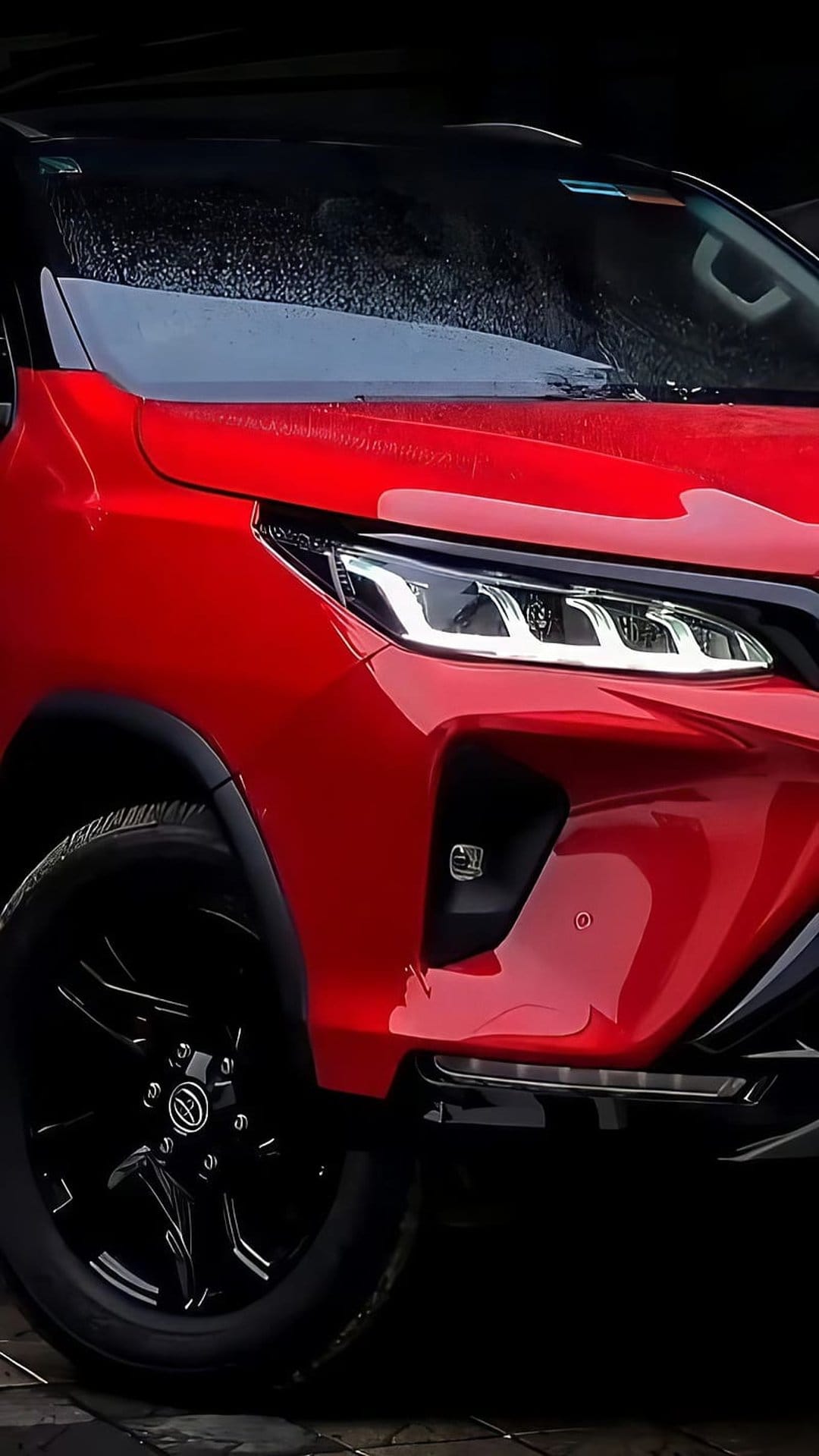 Red Toyota Fortuner SUV showcasing LED daytime running lights and black wheels against a damp surface.