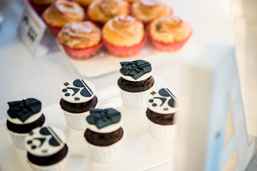 Chocolate cupcakes with white fondant music notes and black bows sit before a tray of glazed cinnamon rolls.