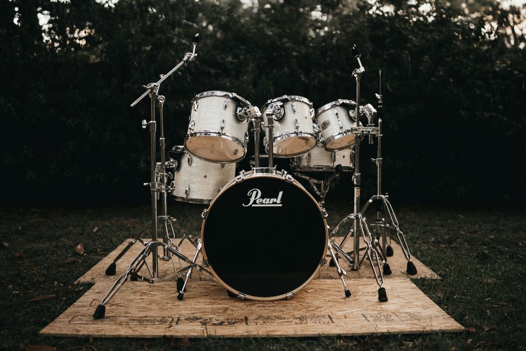 White Pearl drum set on a wooden deck surrounded by green grass and dense dark foliage in natural light.