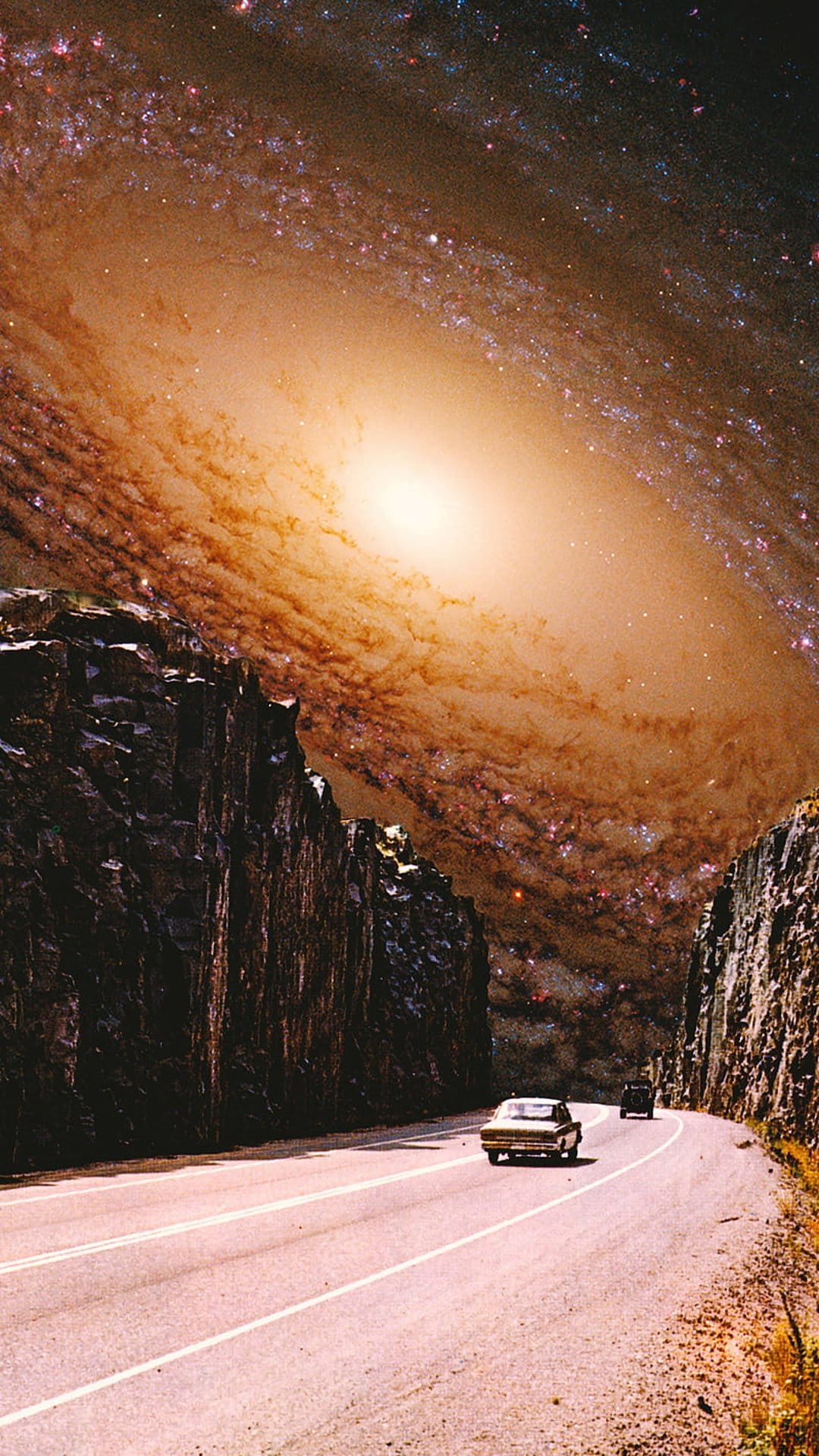 Car driving on a winding road through a canyon toward a massive purple spiral galaxy in the starry night sky.