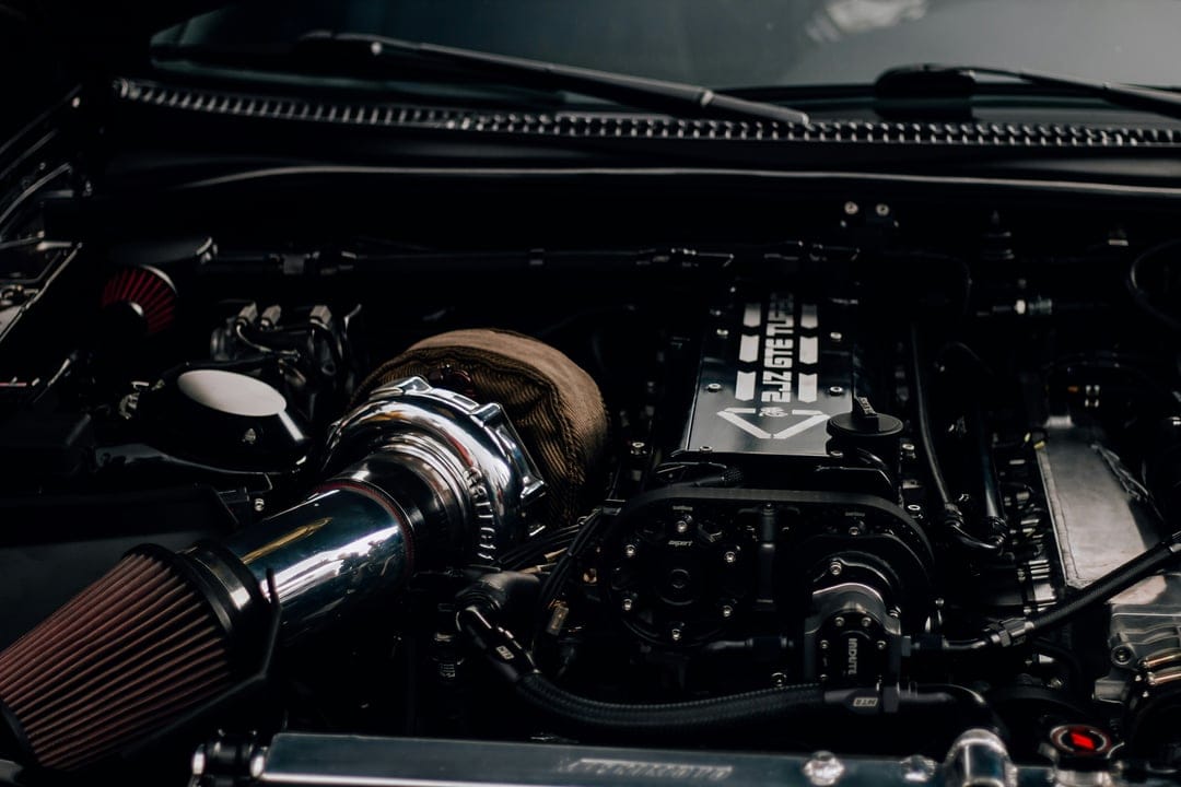 Chrome turbocharger with heat-wrapped piping and a red intake filter inside a dark modified car engine bay.