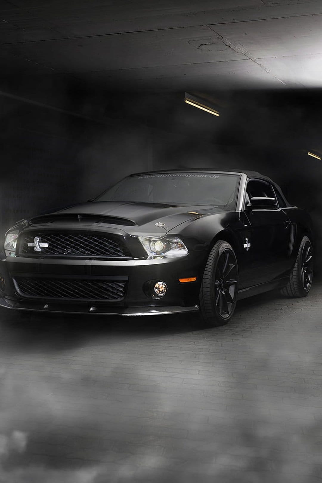 Black Ford Mustang Shelby GT500 parked in a misty garage with glowing headlights and aggressive front grille.