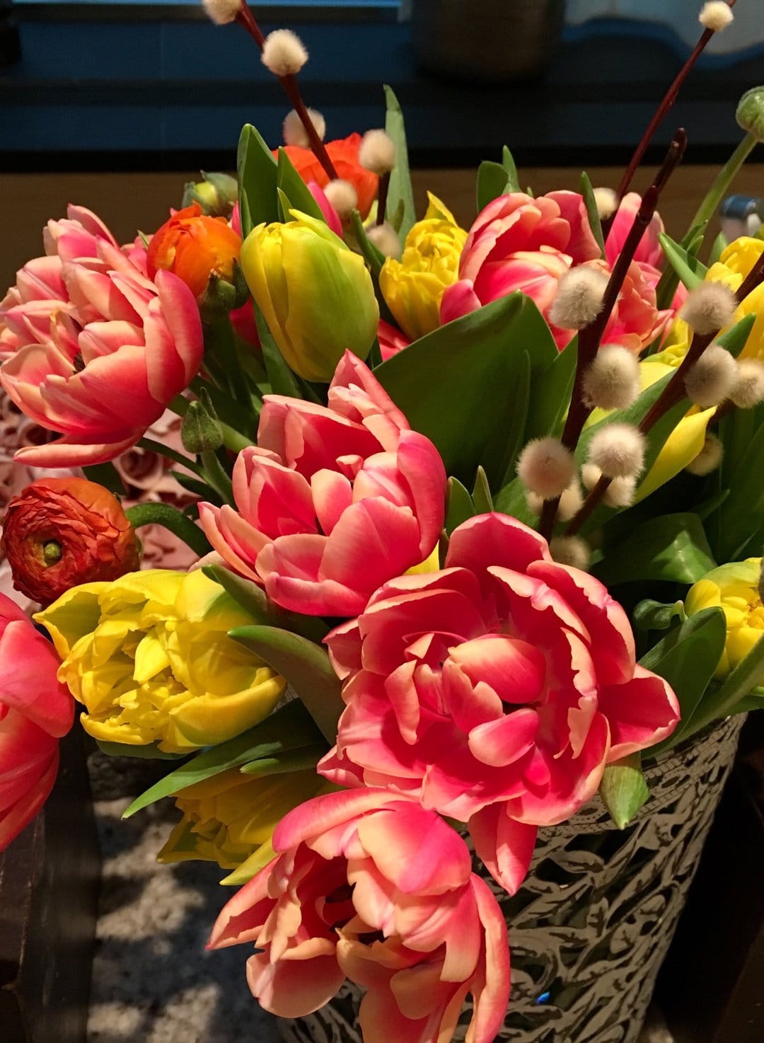 Pink and yellow double tulips mixed with fuzzy pussy willow catkins in a close-up seasonal spring floral bouquet.