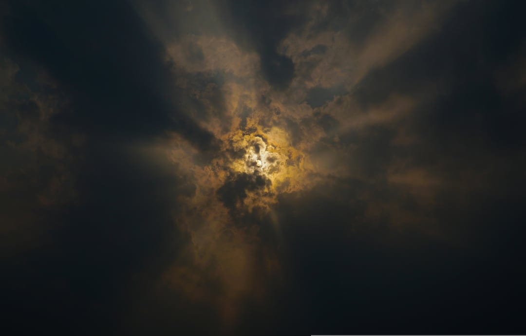 Golden sunbeams pierce through heavy dark storm clouds in a high-contrast, dramatic sky composition.